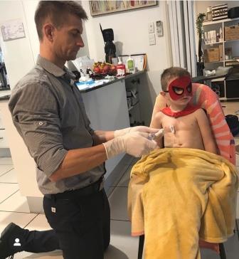 Father preparing infusion for little son dressed in superpower outfit