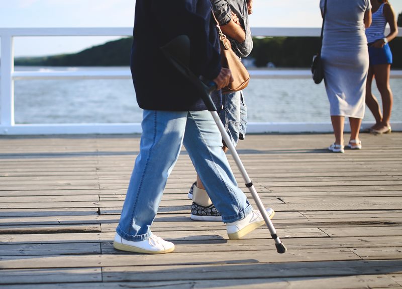 older adult walking along a pier with an elbow crutch